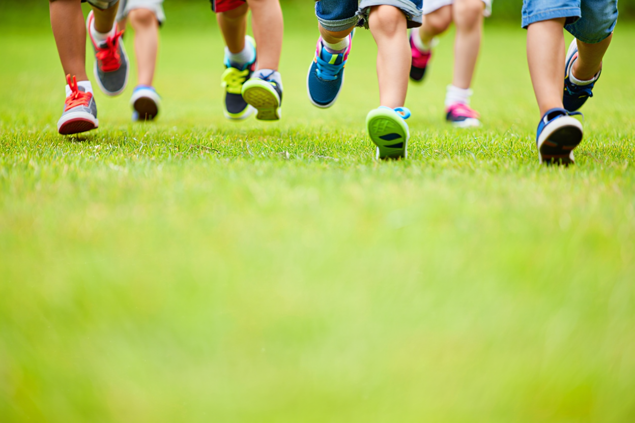 Children's feet in colorful sneakers mid-step on grass, slow-motion race game